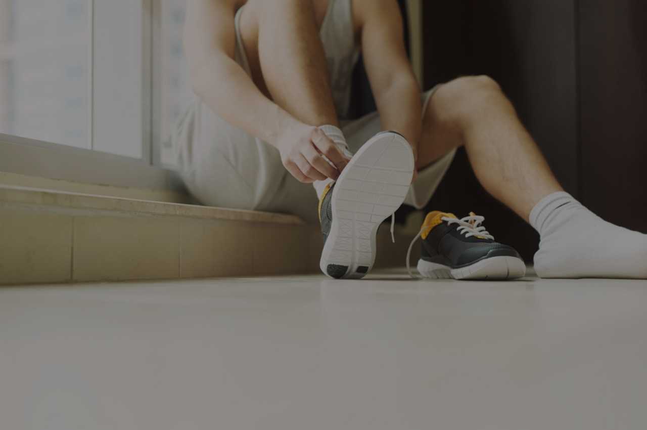 Man putting his shoes on while sitting on the floor while thinking about athletes foot spread